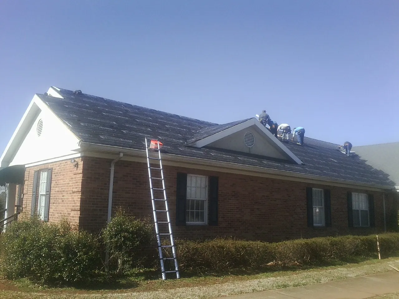 Crew tearing shingles off a brick ranch roof with a ladder set — Metal Roof Repair work by our crew in Schooleys Mountain