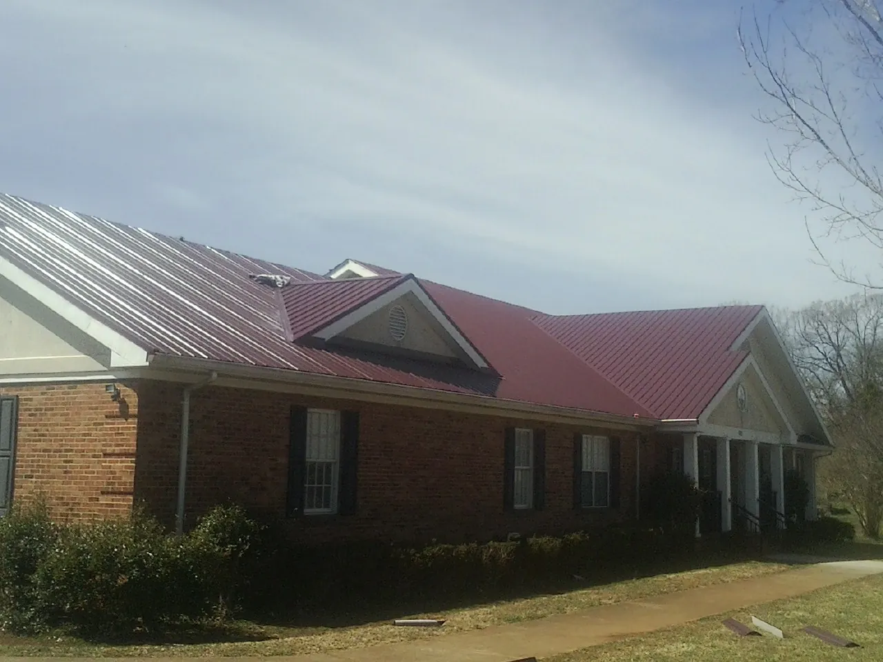 Red metal roof with gabled entries on a long brick building, from a Hail Damage Roof Repair job in Schooleys Mountain