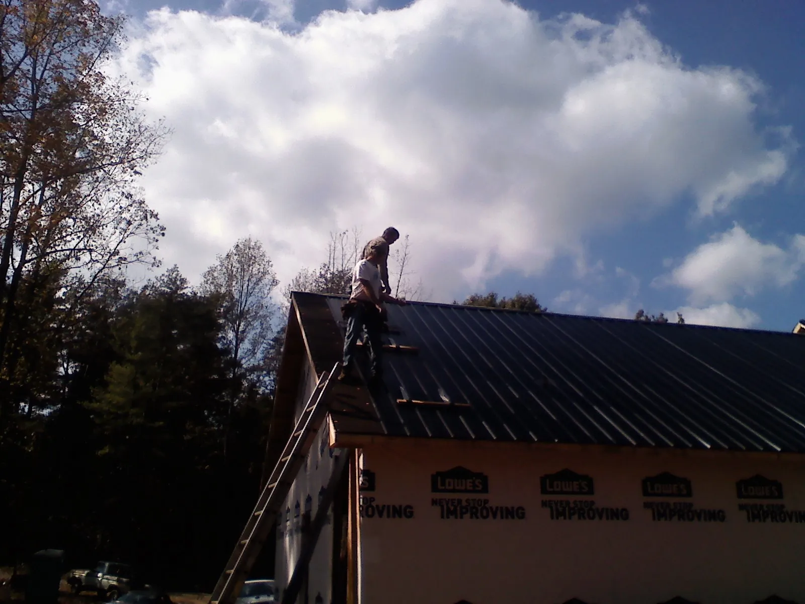 Roofer fastening dark metal panels high against a cloudy sky, from a Roof Inspection job in Schooleys Mountain